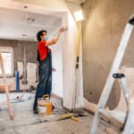 Construction worker plastering and smoothing concrete wall in room. Renovating apartment.